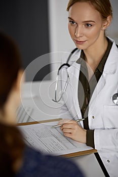 Cheerful smiling female doctor and patient woman discussing current health examination while sitting in clinic. Perfect