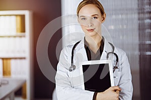 Cheerful smiling female doctor using clipboard in clinic. Portrait of friendly physician woman at work. Medical service