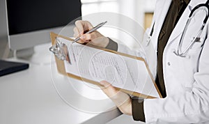 Cheerful smiling female doctor using clipboard in clinic. Portrait of friendly physician woman at work place. Perfect