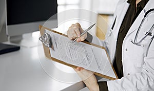 Cheerful smiling female doctor using clipboard in clinic. Portrait of friendly physician woman at work place. Perfect