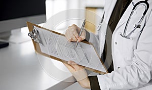 Cheerful smiling female doctor using clipboard in clinic. Portrait of friendly physician woman at work place. Perfect