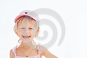 A cheerful, smiling little girl in a rose-colored hat narrowed her eyes