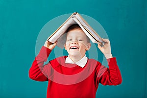 Cheerful smiling little school boy with big books on his head ha