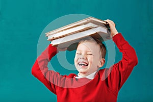 Cheerful smiling little school boy with big books on his head ha