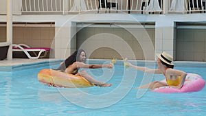 Cheerful smiling multiracial female friends Caucasian girl and Hispanic young woman having fun relaxing in pool of