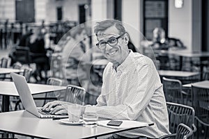 Cheerful smiling old man working on computer while having coffee in terrace coffee shop city outdoors in seniors using modern