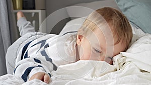 Cheerful smiling toddler boy relaxing in bed at morning. Happy kids, resting at home.