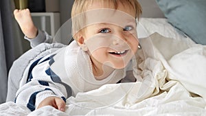 Cheerful smiling toddler boy relaxing in bed at morning. Happy kids, resting at home