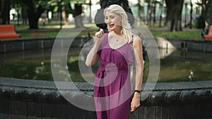 Cheerful smiling woman making wish throwing coin in fountain in park. Portrait of positive beautiful adult Caucasian