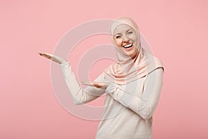 Cheerful smiling young arabian muslim woman in hijab light clothes posing isolated on pink background in studio. People