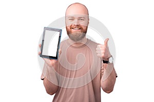 Cheerful smiling young man with beard showing blank screen on tablet and thumb up over white background