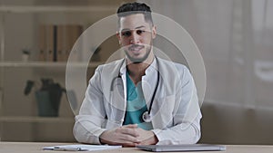 Cheerful smiling young man general practitioner doctor with stethoscope talking at camera explaining diagnosis details