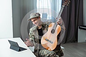 Cheerful smiling young military man wearing khaki uniform holding guitar.