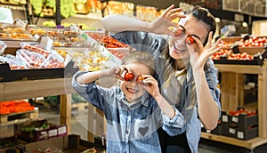 Cheerful smiling young woman with little daughter buying globe tomatoes at the market