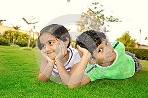 Cheerful south Asian boy and girl lying down in a lawn