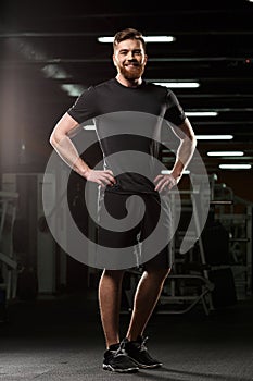 Cheerful sports man standing and posing in gym