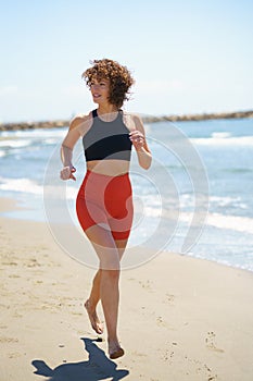 Cheerful sportswoman running on sandy beach and exercising