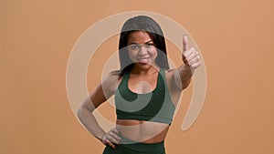 Cheerful Sporty African Woman Gesturing Thumbs-Up Approving Workout, Beige Background