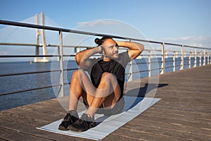 Cheerful sporty guy exercising on pier outdoors next to sea