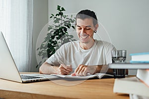 Cheerful student making notes from laptop while online learning