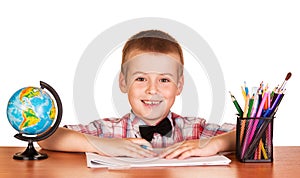 Cheerful student sitting at table, crayons and globe isolated.