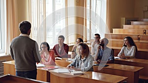 Cheerful students are raising hands to answer teacher`s questions, professor bearded man is pointing at young people and