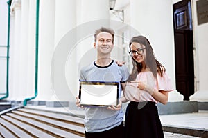 Cheerful students showing laptop with copy space