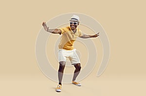 Cheerful stylish african american man having fun dancing on light beige background.