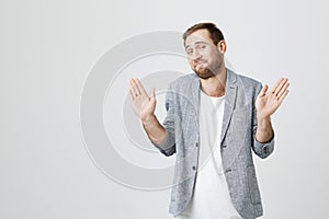 Cheerful stylish fashionable bearded guy in trendy jacket over white t-shirt raises hands as shows being uninvolved, has
