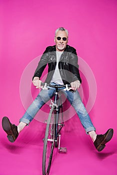 Cheerful stylish senior man wearing leather jacket riding bicycle