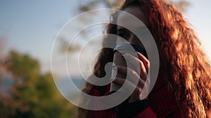 Cheerful stylish young woman in red coat scarf standing outdoors on the street drinking coffee in sunshine light in