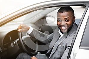 Cheerful successful black businessman looking through car window