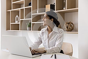 Cheerful successful young Indian manager woman using laptop in office