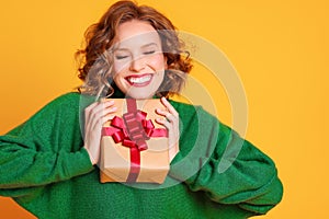 Cheerful surprised   woman  laughs with closed eyes holds a Christmas gifts on a colored yellow background photo