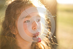 A cheerful sweet girl with cherry berries in her mouth. Funny summer portrait of a child with a cherry, gifts of summer, summer