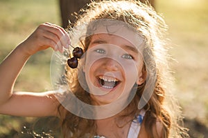 A cheerful sweet girl with cherry berries in her mouth. Funny summer portrait of a child with a cherry, gifts of summer, summer