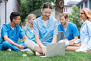 cheerful teacher and multicultural students studying outdoors with gadgets