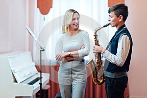 Cheerful teacher with student boy learning saxophone lessons at school