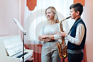 Cheerful teacher with student boy learning saxophone lessons at school
