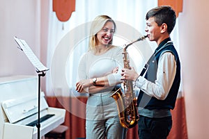 Cheerful teacher with student boy learning saxophone lessons at school