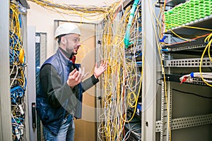 Cheerful technician waves his hand in the data center.  An engineer in a white helmet is happy with his work in the server room.