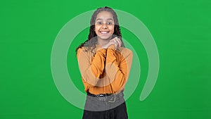 Cheerful teen African American girl waving looking at camera posing at green screen. Portrait of positive smiling