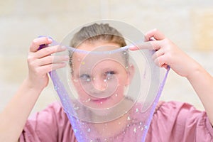 Cheerful teen girl holding a purple slime and looking through.