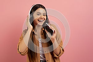Cheerful teen girl listening music in wireless headphones and singing