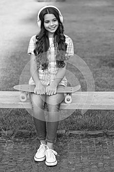 cheerful teen girl with skateboard in headphones. teen girl with skateboard outside. teen girl with skateboard listen photo