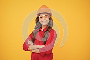 cheerful teen girl wear eyeglasses and helmet. kid future engineer on yellow background.