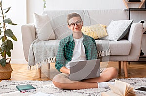 Cheerful teen guy doing homework, using laptop