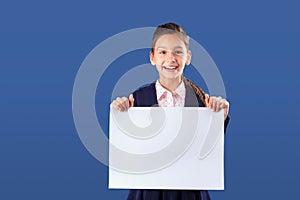 Cheerful teenage girl holding white card with copy space on blue background. Mockup for text