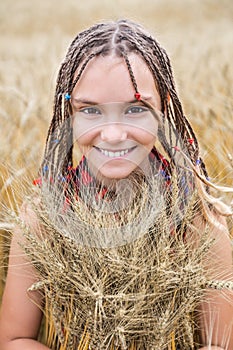 Cheerful teenage girl with pigtails smiles and hugs ripe wheat in the field