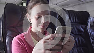 Cheerful teenage girl plays a game on smartphone in the cabin of the plane while traveling stock footage video